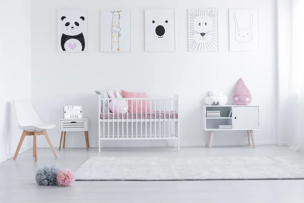 Pink cushions in cradle and chair in white child's room interior with posters and carpet. Real photo — Stock Photo, Image