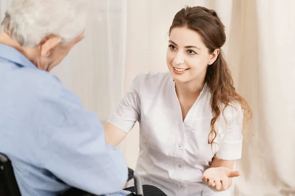 Junge hilfsbereite Ärztin mit älterem Mann im Rollstuhl — Stockfoto