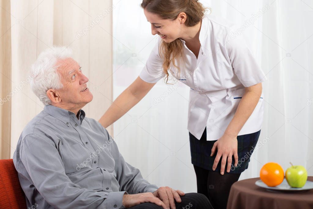 Old man in nursing home with helpful carer at his side