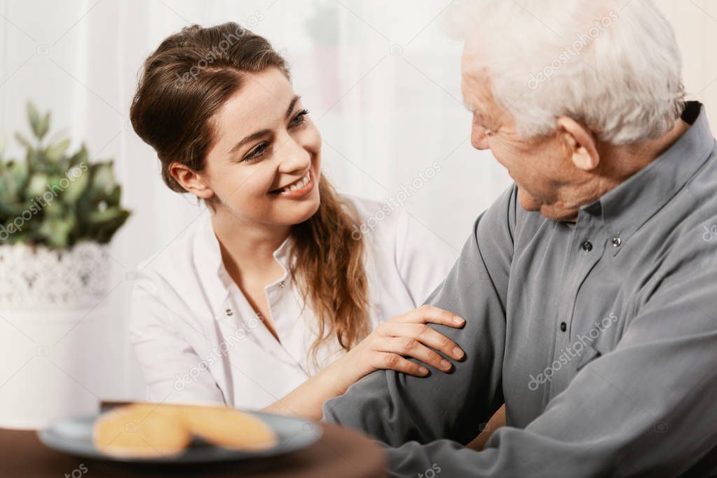 Smiling young nurse sitting at table with senior patient