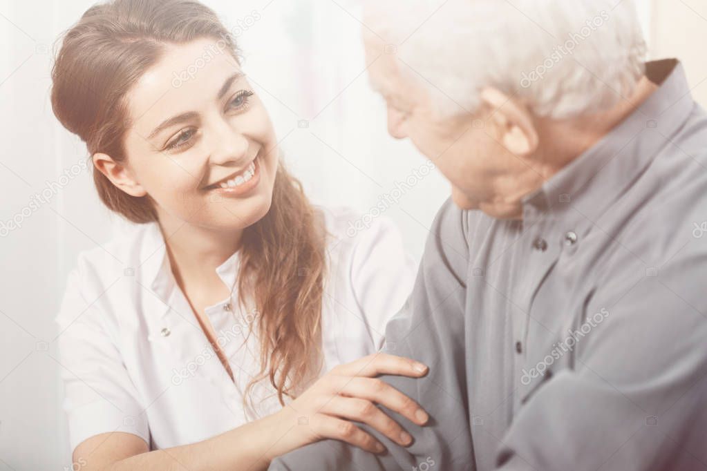 Beautiful volunteer smiling at senior man at nursing home