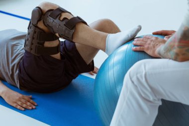 Spor salonunda mavi paspasın üzerinde oturan ve topla antrenman yapan hoş bir hasta.