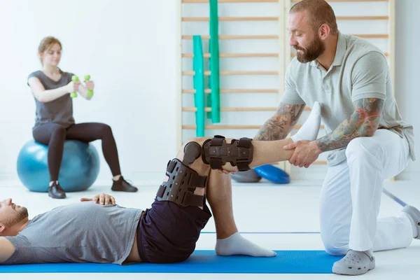 Dospívající dívka po autonehodě s ortézou na nohou cvičení na modré podložce ve společnosti fyzioterapeuta — Stock fotografie