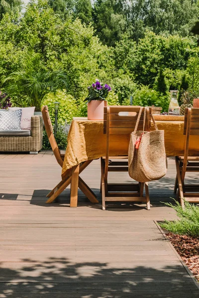 Mesa de comedor cubierta con mantel naranja de pie en terraza de madera en jardín verde —  Fotos de Stock