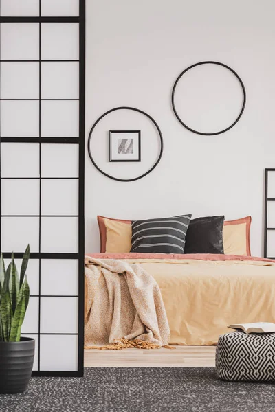 Schwarze Reifen an einer weißen Wand in einem eleganten Schlafzimmer mit orangefarbener Bettwäsche auf dem Bett — Stockfoto