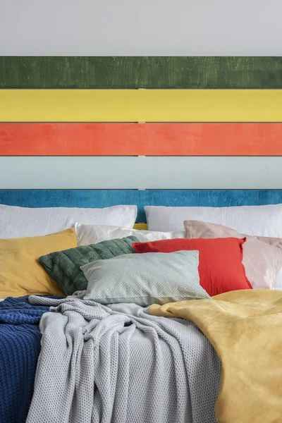 Close up of king size bed with green, yellow, red and grey pillows — стоковое фото