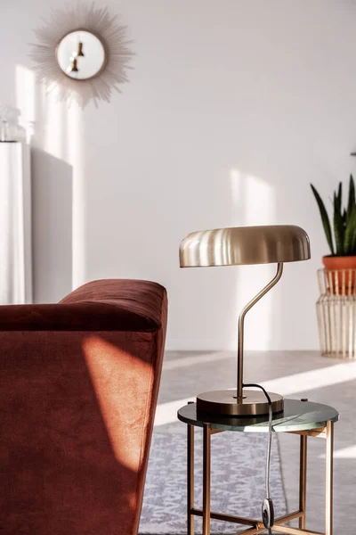 Elegante lámpara dorada en una elegante mesa auxiliar junto a un cómodo sofá en el interior de la sala de estar de moda — Foto de Stock
