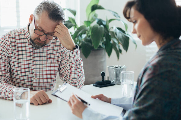 Handsome worried man sitting at a desk in front of his professional therapist