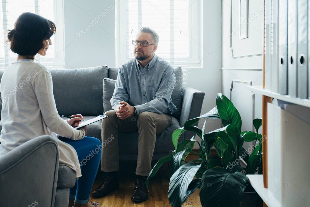 Handsome man sitting on a gray sofa during a meeting with a psychotherapist