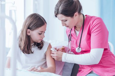 Pembe üniformalı doktor hastanede bir çocuğa iğne yapıyor.