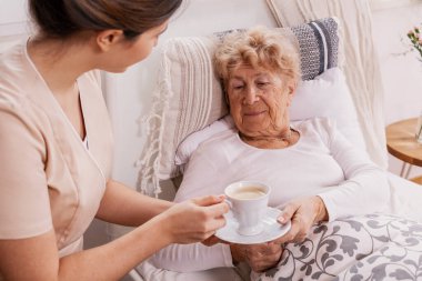 Genç ve güzel hemşire, özel bir bakımevinde yaşlı bir bayana çay ikram ediyor.