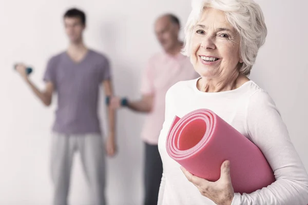 Happy Senior Žena Držení Růžová Joga Mat Muži Cvičení Pozadí — Stock fotografie