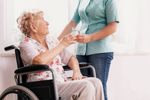 Профессиональная Медсестра Синей Форме Дает Стакан Воды Пожилой Женщине Инвалидном Лицензионные Стоковые Изображения