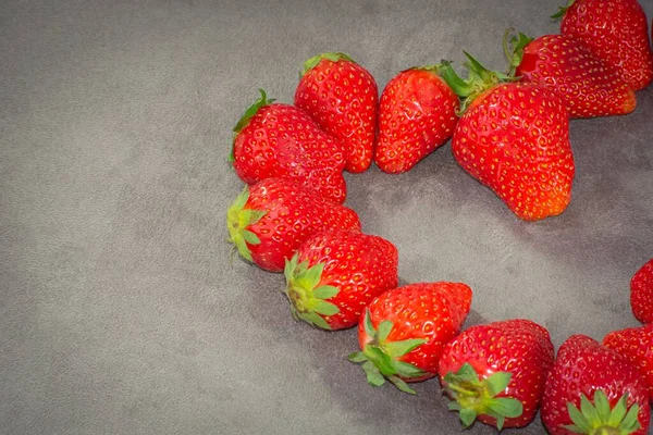 Olgun çilekler, gri bir arka planda yarım kalp şeklinde serilmiş.
