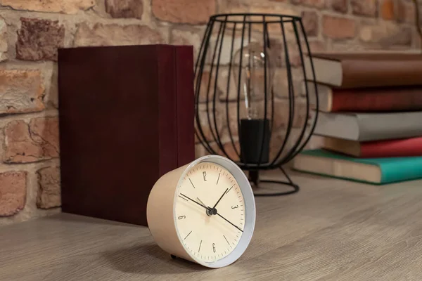 Masanın üzerinde duran dekoratif eşyalar masa saati, kitaplar, parlak bir lambası olan modern bir mum tutacağı.