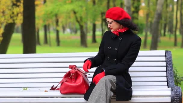 Mooie vrouw met een tas, zittend op bankje in herfst Park. — Stockvideo