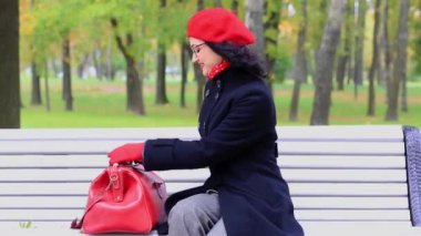 Bir çanta ile güzel kadın, sonbahar parkta bankta oturan.