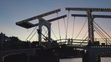 Amsterdam'ın akşam manzarası. Kanallar, aydınlatma ile süslenmiş köprü altından geçen tekne, mimari ve sokak Lambaları.