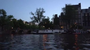 Amsterdam'ın akşam manzarası. Kanallar, aydınlatma ile süslenmiş köprü altından geçen tekne, mimari ve sokak Lambaları.