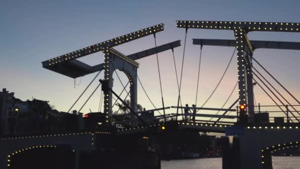 Вечерний вид на Амстердам. Каналы, лодки, проходящие под мостом, украшенные освещением, архитектурой и уличным освещением . — стоковое видео