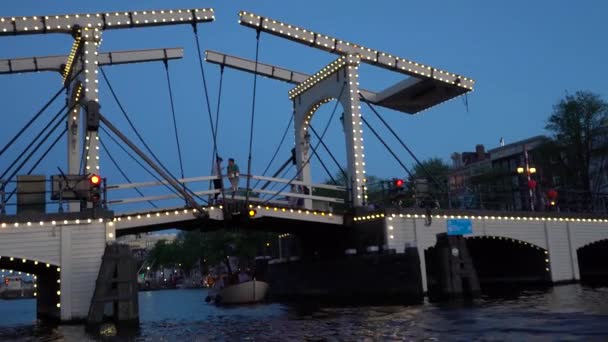 Vista nocturna de Ámsterdam. Canales, barco que pasa por debajo del puente decorado con iluminación, arquitectura y farolas . — Vídeo de stock