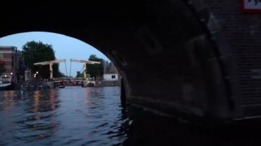 Amsterdam'ın akşam manzarası. Kanallar, aydınlatma ile süslenmiş köprü altından geçen tekne, mimari ve sokak Lambaları.