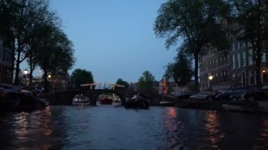 Amsterdam'ın akşam manzarası. Kanallar, aydınlatma ile süslenmiş köprü altından geçen tekne, mimari ve sokak Lambaları.