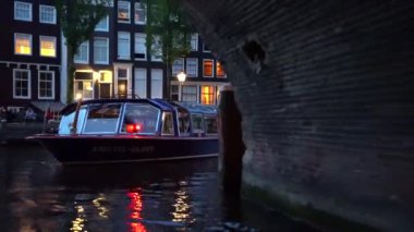 Amsterdam'ın akşam manzarası. Kanallar, aydınlatma ile süslenmiş köprü altından geçen tekne, mimari ve sokak Lambaları.