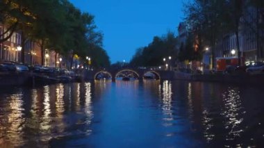 Amsterdam'ın akşam manzarası. Kanallar, aydınlatma ile süslenmiş köprü altından geçen tekne, mimari ve sokak Lambaları.
