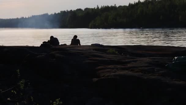 Deux silhouettes d'un homme qui allume un feu sur le lac le soir — Video