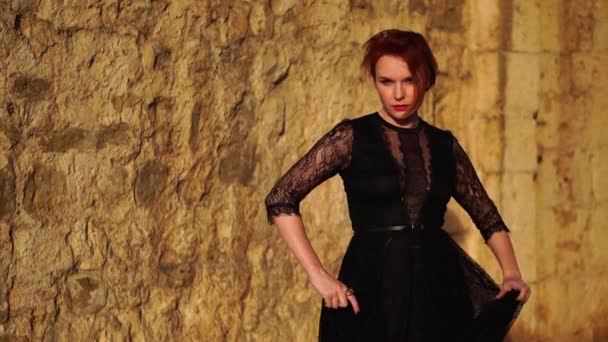 Charmante vrouw met rode horen in de avond zwarte jurk maken dansen bewegingen tegen de gele muur van de oude stad — Stockvideo