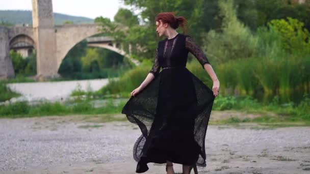 Чарівна жінка з червоним чути ввечері чорне плаття робить танцюючі рухи в старому місті — стокове відео