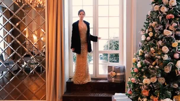 Ein schönes Mädchen im Abendkleid und schwarzem Nerzmantel kommt in den mit einem Weihnachtsbaum geschmückten Raum. — Stockvideo