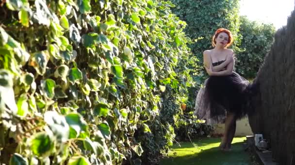 Красива дівчина з білою шкірою і рудим волоссям в саду в сонячний день — стокове відео