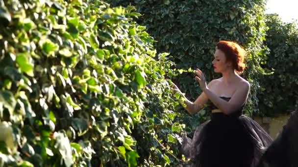 Een mooi meisje met witte huid en rood haar in de tuin op een zonnige dag — Stockvideo