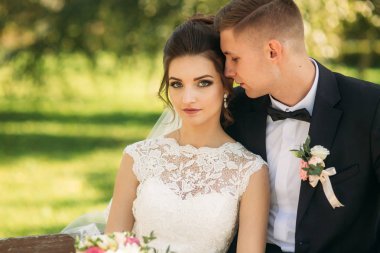 Düğün giysileri içinde genç bir çift bir parkta bir bankta oturuyor. Güneşli havalarda