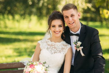 Düğün giysileri içinde genç bir çift bir parkta bir bankta oturuyor. Güneşli havalarda