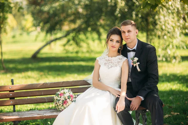Un jeune couple en tenue de mariage est assis sur un banc dans un parc. Météo ensoleillée — Photo