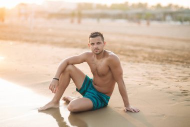 Yakışıklı adam kumlu bir plaj sahil üzerinde oturur