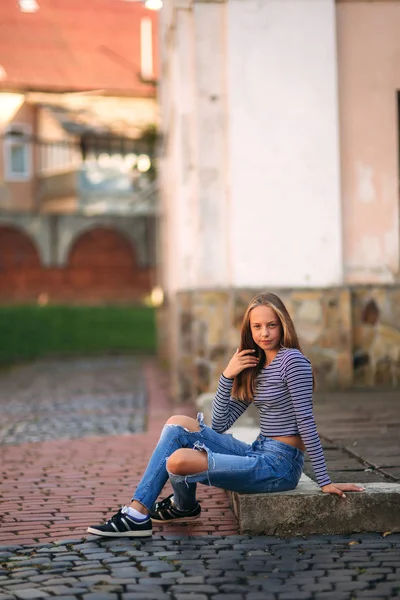 Joven adolescente posa para la foto. chica rubia en jeans y blusa. jugar con el pelo —  Fotos de Stock