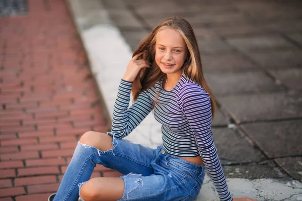 Jonge tiener houdingen voor foto. blond meisje in spijkerbroek en blouse. spelen met haar — Stockfoto