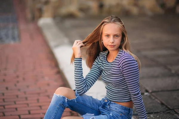 Jonge tiener houdingen voor foto. blond meisje in spijkerbroek en blouse. spelen met haar — Stockfoto