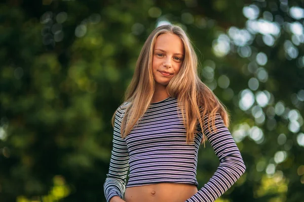 Blondes Teenager-Mädchen in gestreifter Bluse auf dem Hintergrund eines grünen Baumes — Stockfoto