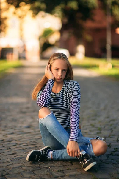 一个穿着牛仔裤和衬衫的十几岁的女孩坐在街道的中间 — 图库照片