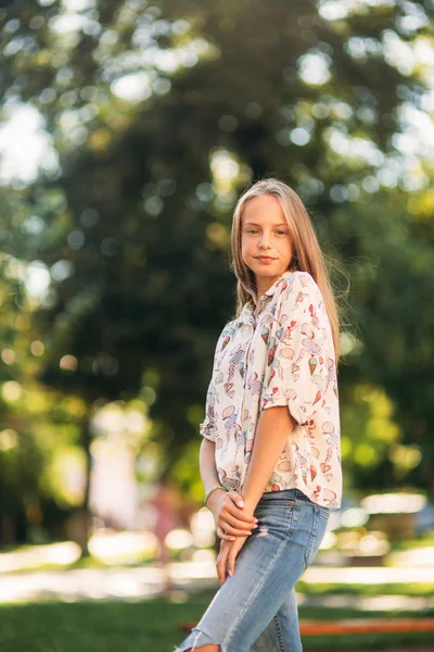 Blondes Mädchen in Bluse posiert vor dem Hintergrund eines grünen Baumes für Fotografen — Stockfoto