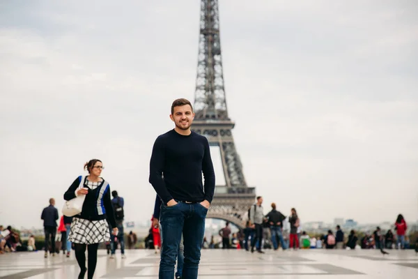 Un bel homme portant un pull bleu foncé est debout sur le fond de la Tour Eiffel — Photo