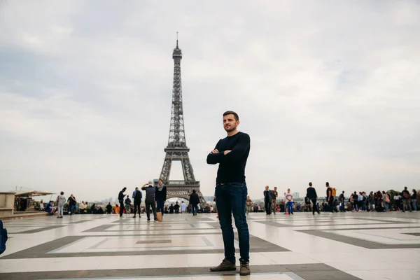 Un bel homme portant un pull bleu foncé est debout sur le fond de la Tour Eiffel — Photo