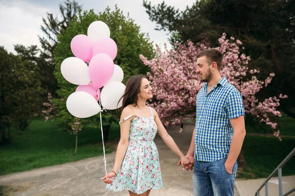 Junges glückliches Paar verliebt im Freien. schöner Mann und schöne Frau bei einem Spaziergang in einem frühlingshaft blühenden Park. sie halten Heliumkugeln — Stockfoto