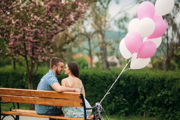 Joven pareja feliz enamorada al aire libre. Hombre guapo y mujer hermosa en un paseo en un parque floreciente primavera. Mantienen bolas de helio. —  Fotos de Stock