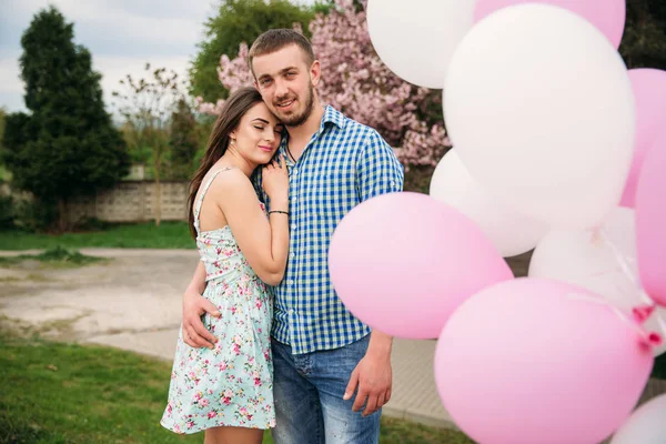 Jonge gelukkige paar verliefd buitenshuis. Knappe man en mooie vrouw op een wandeling in een bloeiende lente-park. Ze houden helium ballen — Stockfoto